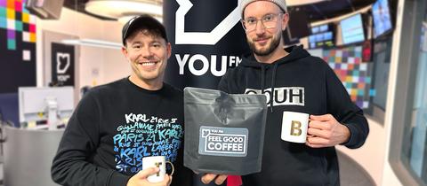 Benne und Timo halten ein Päckchen YOU FM Feel Good Coffee in die Kamera.