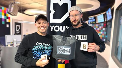 Benne und Timo halten ein Päckchen YOU FM Feel Good Coffee in die Kamera.