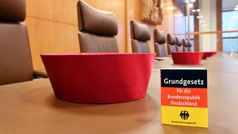 Auf der Richterbank im Sitzungssaal im Bundesverfassungsgericht liegen Barette der Bundesverfassungsrichter des ersten Senats. Dabei ist eine Miniaturausgabe des Grundgesetz für die Bundesrepublik Deutschland zu sehen.